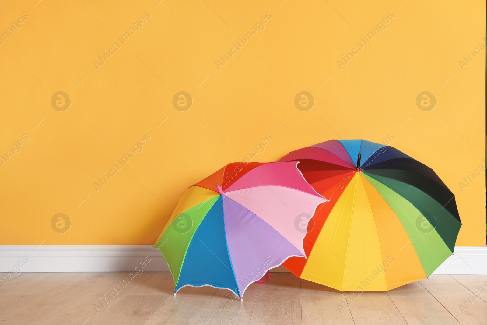 Photo of Beautiful open umbrellas on floor near color wall with space for design