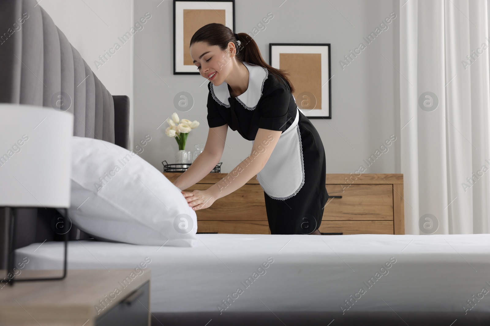 Photo of Young chambermaid making bed in hotel room