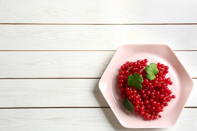 Photo of Delicious red currants and leaves on white wooden table, top view. Space for text