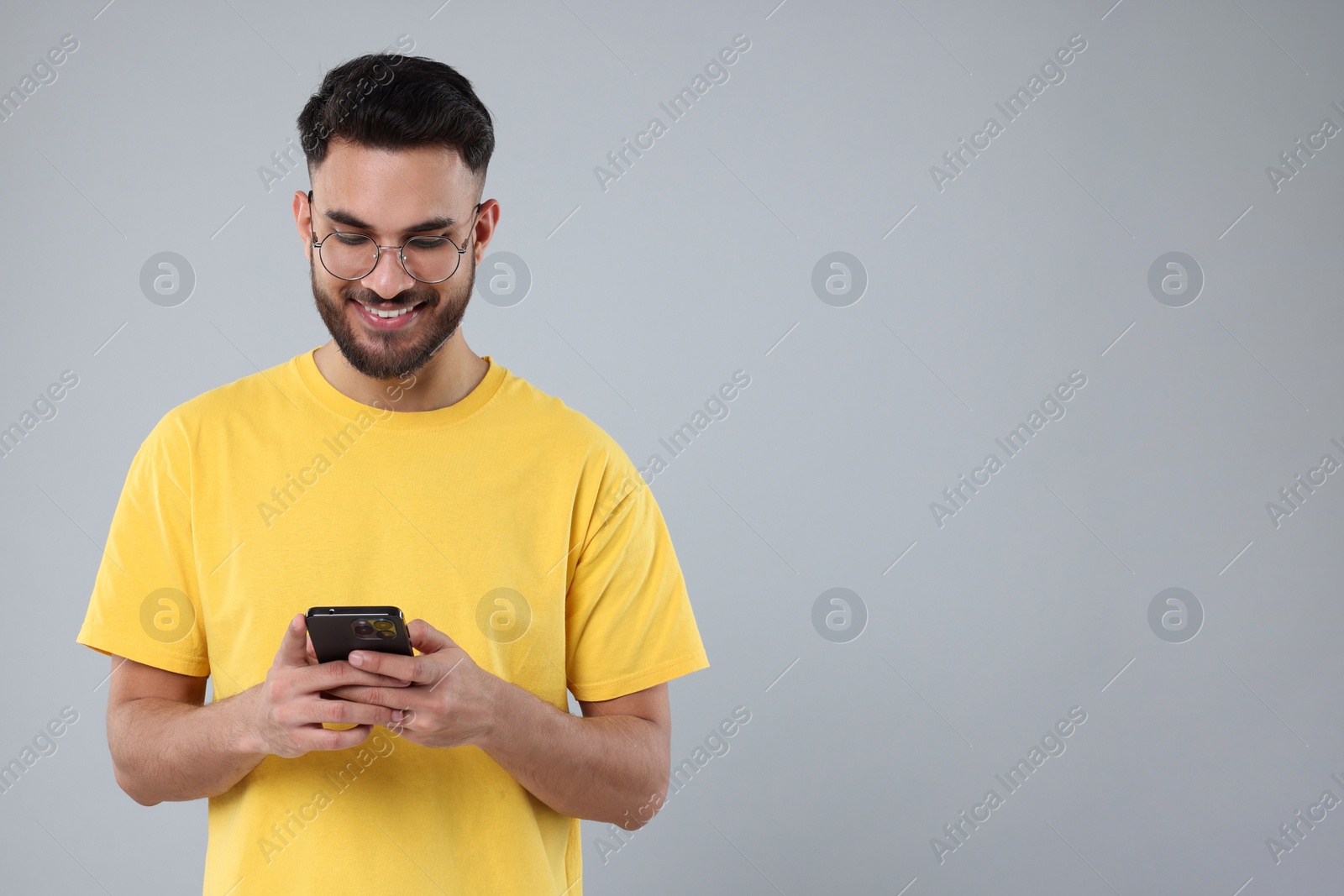 Photo of Happy young man using smartphone on grey background, space for text