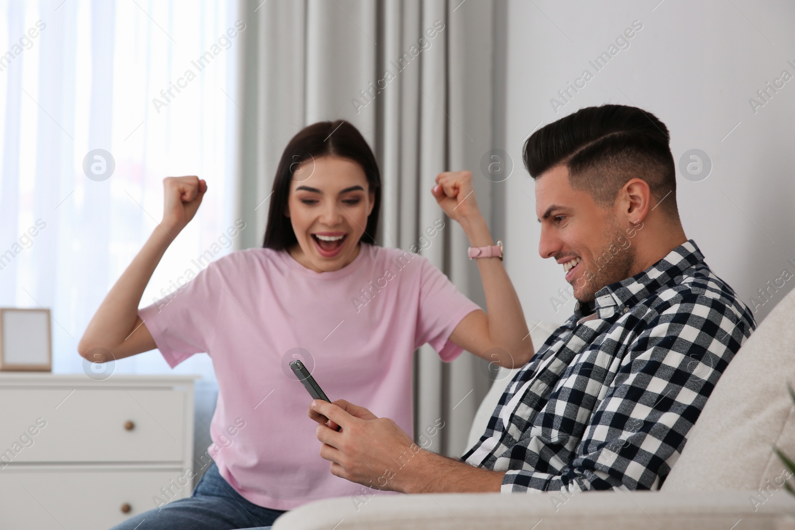 Photo of Emotional couple participating in online auction using smartphone at home