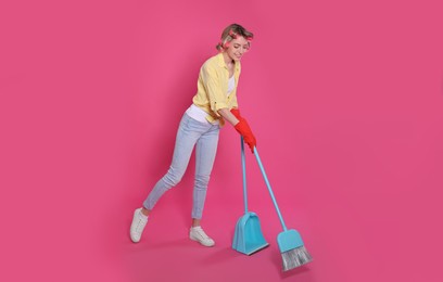 Young housewife with broom and dustpan on pink background