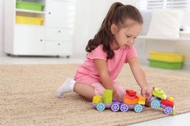 Cute little girl playing with toys on floor at home, space for text