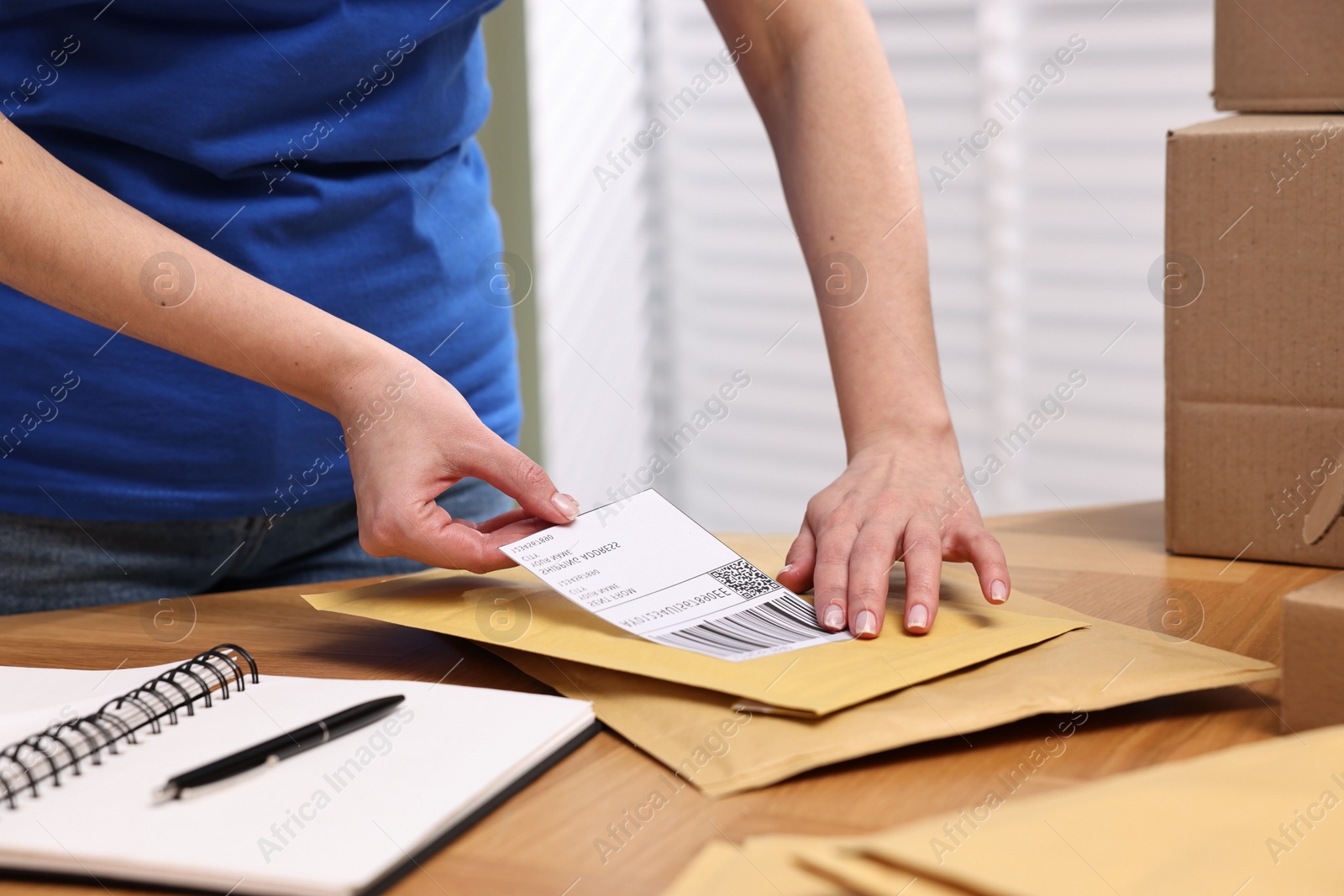 Photo of Parcel packing. Post office worker sticking barcode on bag at wooden table indoors, closeup