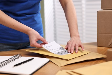 Photo of Parcel packing. Post office worker sticking barcode on bag at wooden table indoors, closeup