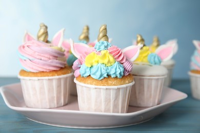 Plate with cute sweet unicorn cupcakes on light blue wooden table