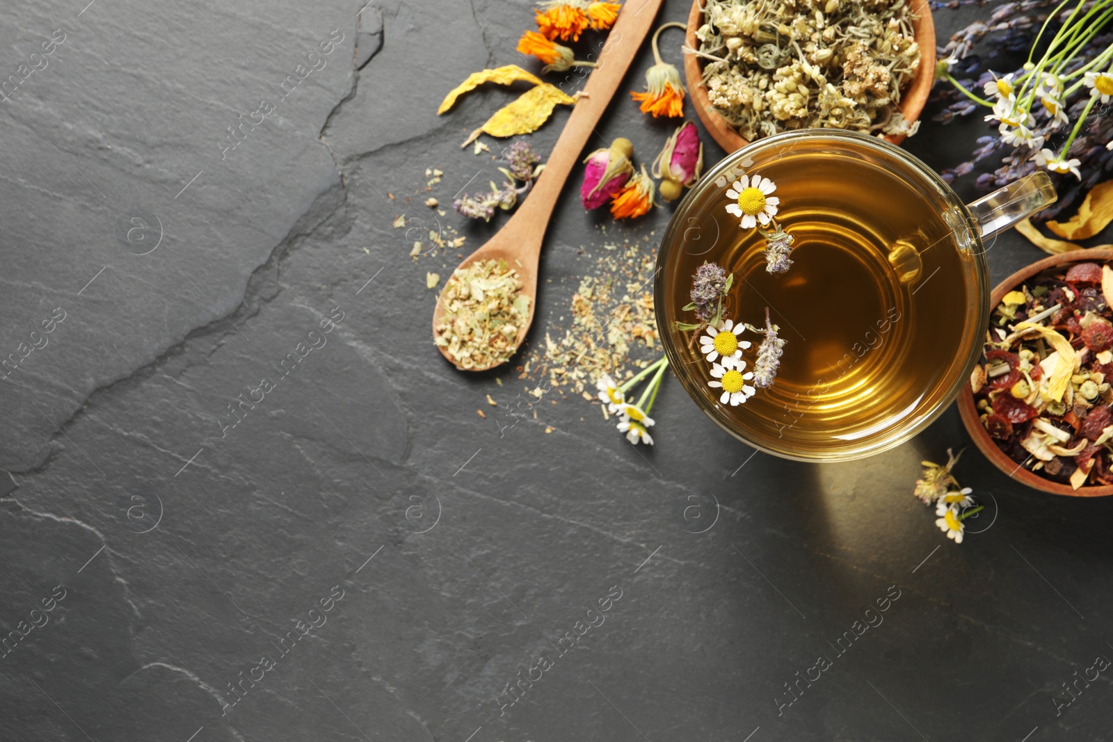 Photo of Glass cup of aromatic freshly brewed tea near different dry herbs on black table, flat lay. Space for text