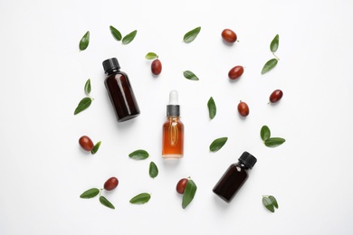 Glass bottles with jojoba oil and seeds on white background, top view
