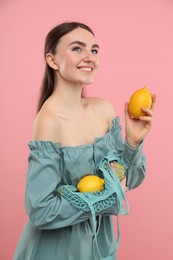 Woman with string bag of fresh lemons on pink background