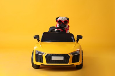 Photo of Funny pug dog with sunglasses in toy car on yellow background