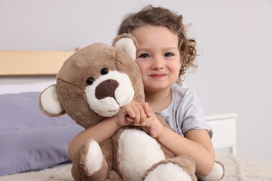 Photo of Cute little girl with teddy bear on bed indoors