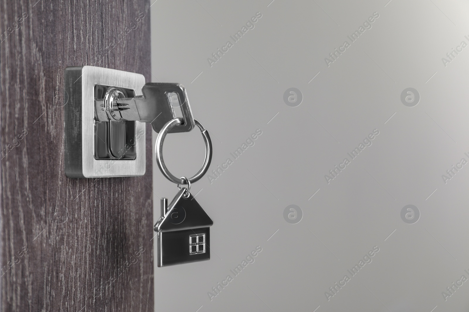 Photo of Mortgage and real estate. Open door with key and house shaped keychain against light background, space for text