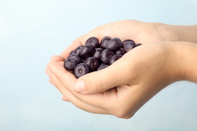 Photo of Female holding fresh acai berries on light blue background, closeup view