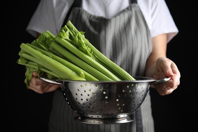 Woman holding colander with fresh green celery on black background, closeup