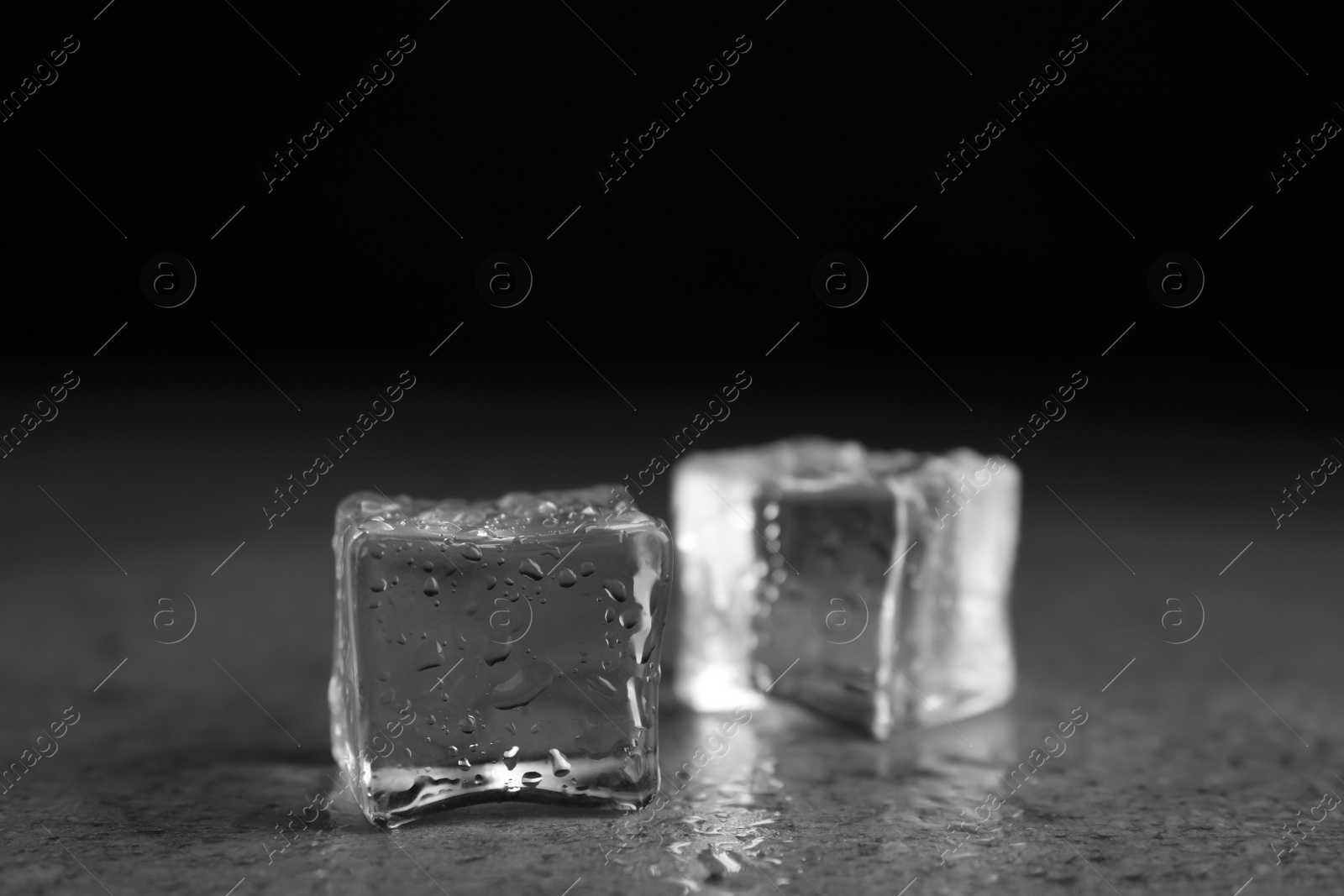 Photo of Ice cubes with water drops on grey stone table, closeup