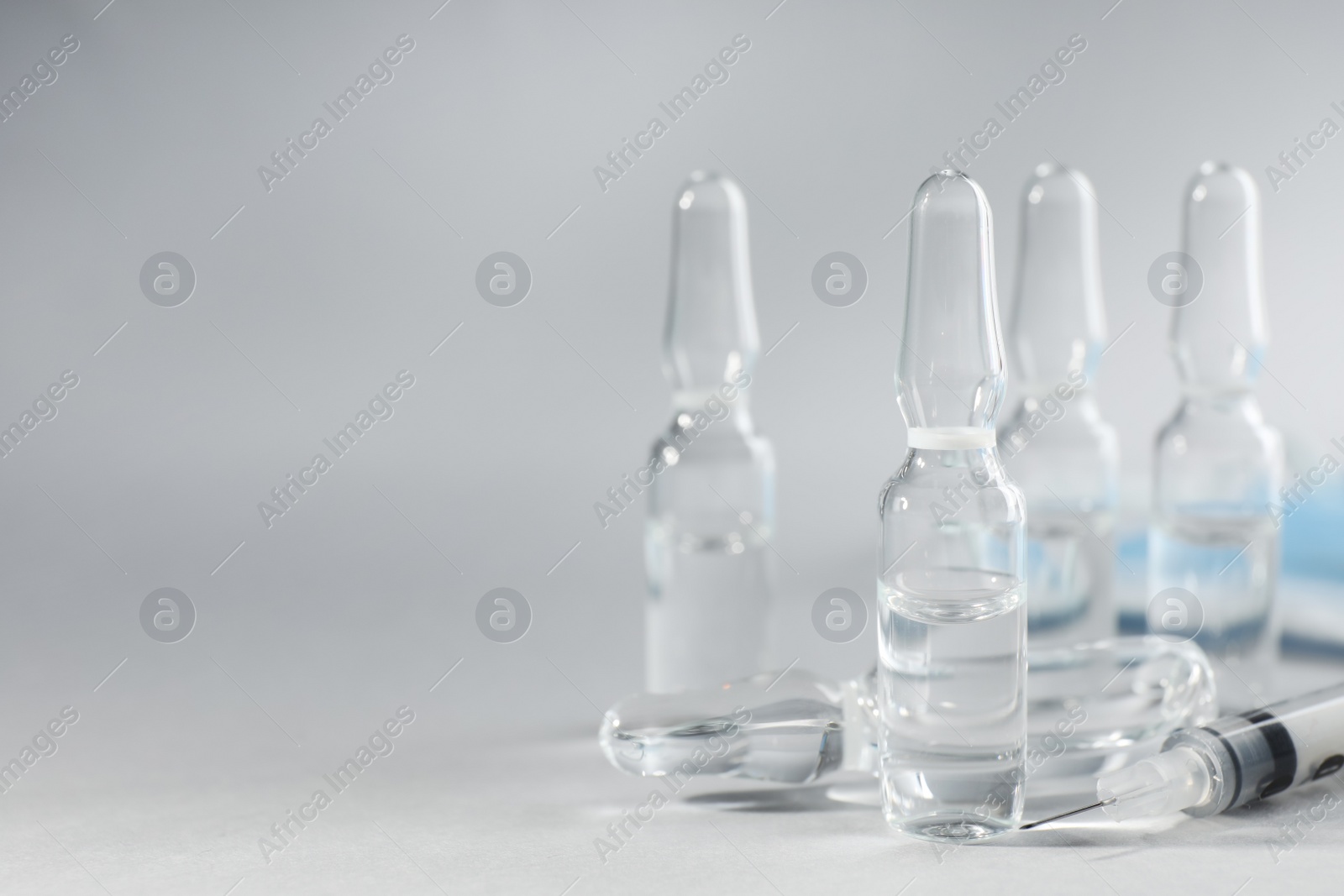 Photo of Pharmaceutical ampoules and syringe on light grey background. Space for text