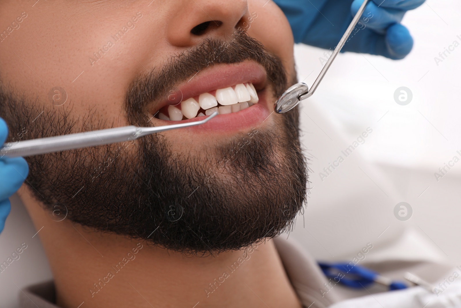 Photo of Dentist examining young man's teeth in clinic, closeup
