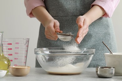 Woman sifting flour into bowl at grey marble table indoors, closeup. Cooking traditional grissini