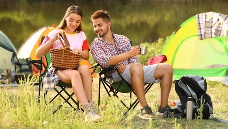 Young couple having picnic near camping tent