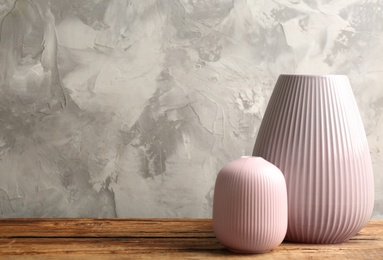 Stylish pink ceramic vases on wooden table against grey background, space for text