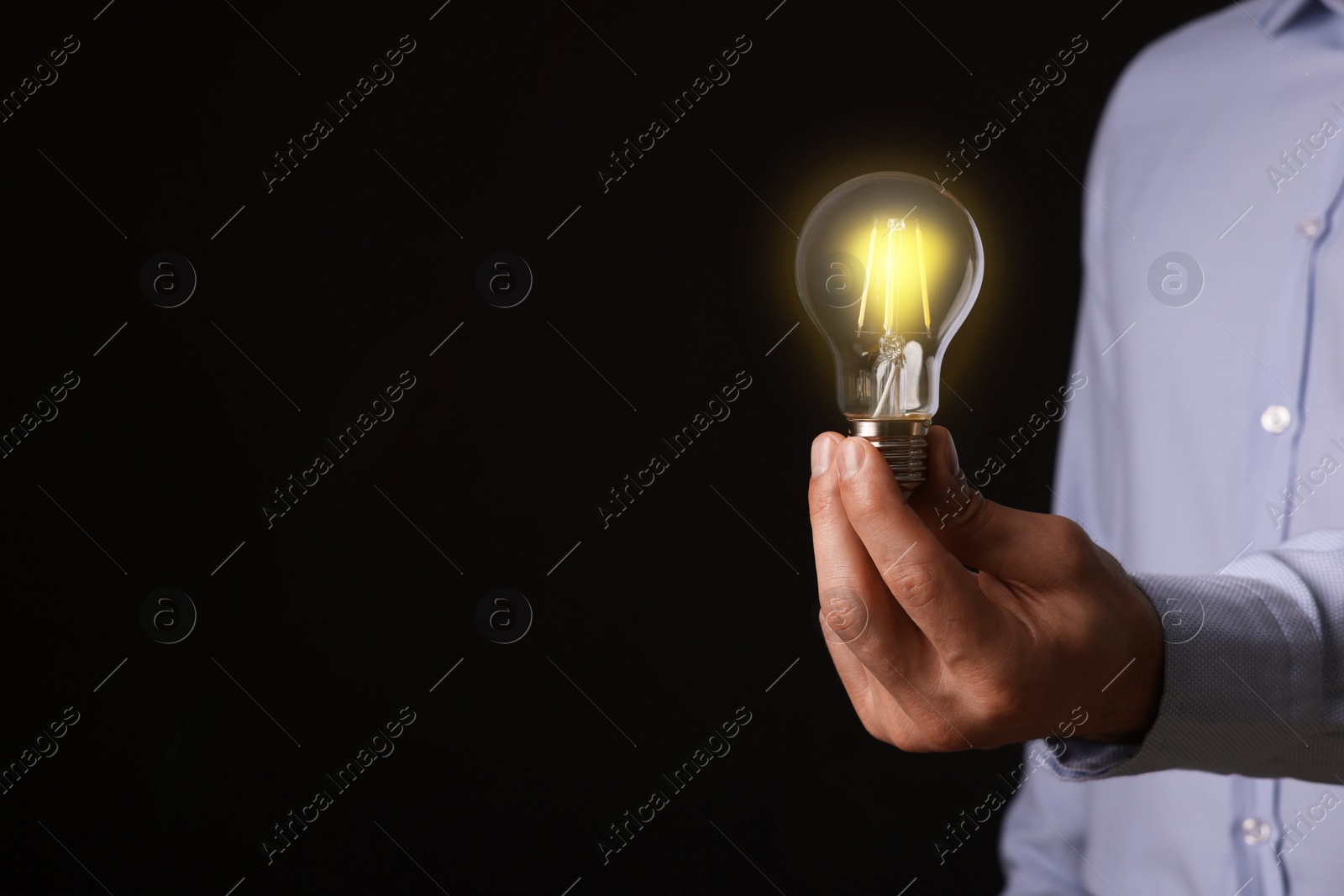 Photo of Glow up your ideas. Closeup view of man holding light bulb on black background, space for text