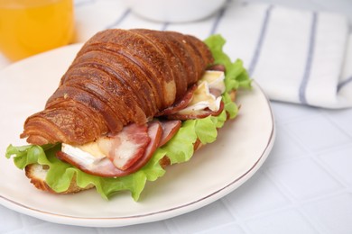 Tasty croissant with brie cheese, ham and bacon on white tiled table, closeup. Space for text