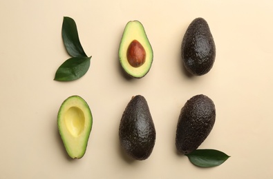 Whole and cut ripe avocadoes with green leaves on beige background, flat lay