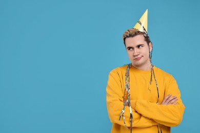 Sad young man with party hat on light blue background, space for text