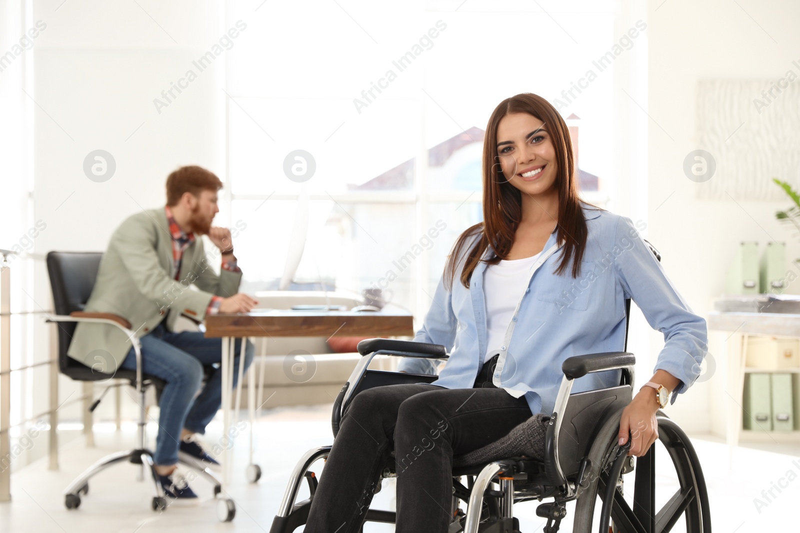 Photo of Young woman in wheelchair with colleague at office