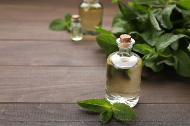 Photo of Bottle of essential oil and mint on wooden table. Space for text