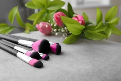 Makeup brushes and flowers on grey table