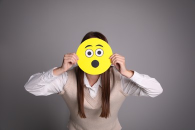 Photo of Woman covering face with shocked emoji on grey background