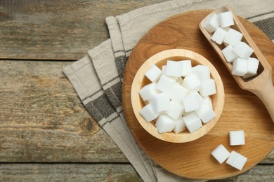 Photo of White sugar cubes in bowl and scoop on wooden table, top view. Space for text