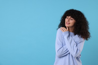 Photo of Happy young woman in stylish warm sweater on light blue background, space for text