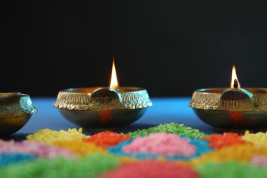 Photo of Diwali celebration. Diya lamps and colorful rangoli on table against black background, closeup