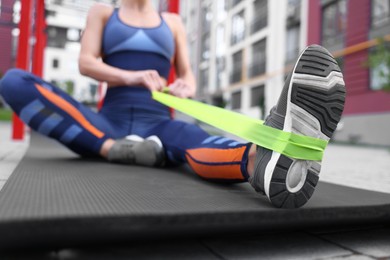 Woman doing exercise with fitness elastic band on mat outdoors, closeup