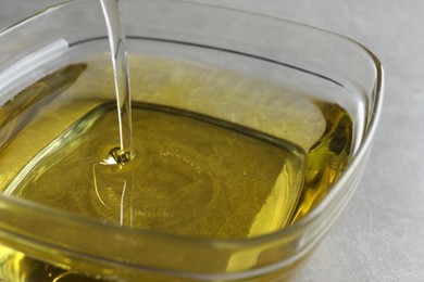 Photo of Pouring cooking oil into bowl on light background, closeup