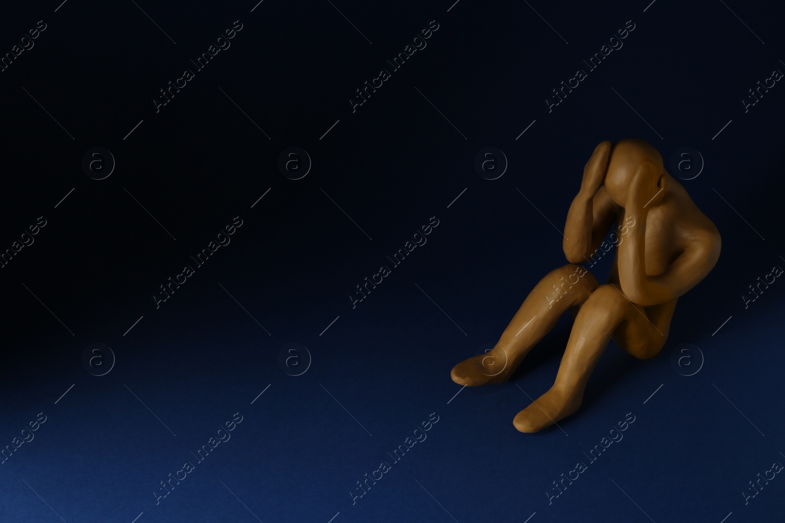 Photo of Plasticine figure of crying human on dark blue background. Space for text