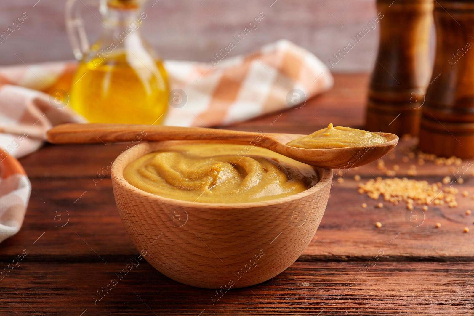 Photo of Bowl and spoon with tasty mustard sauce on wooden table, closeup