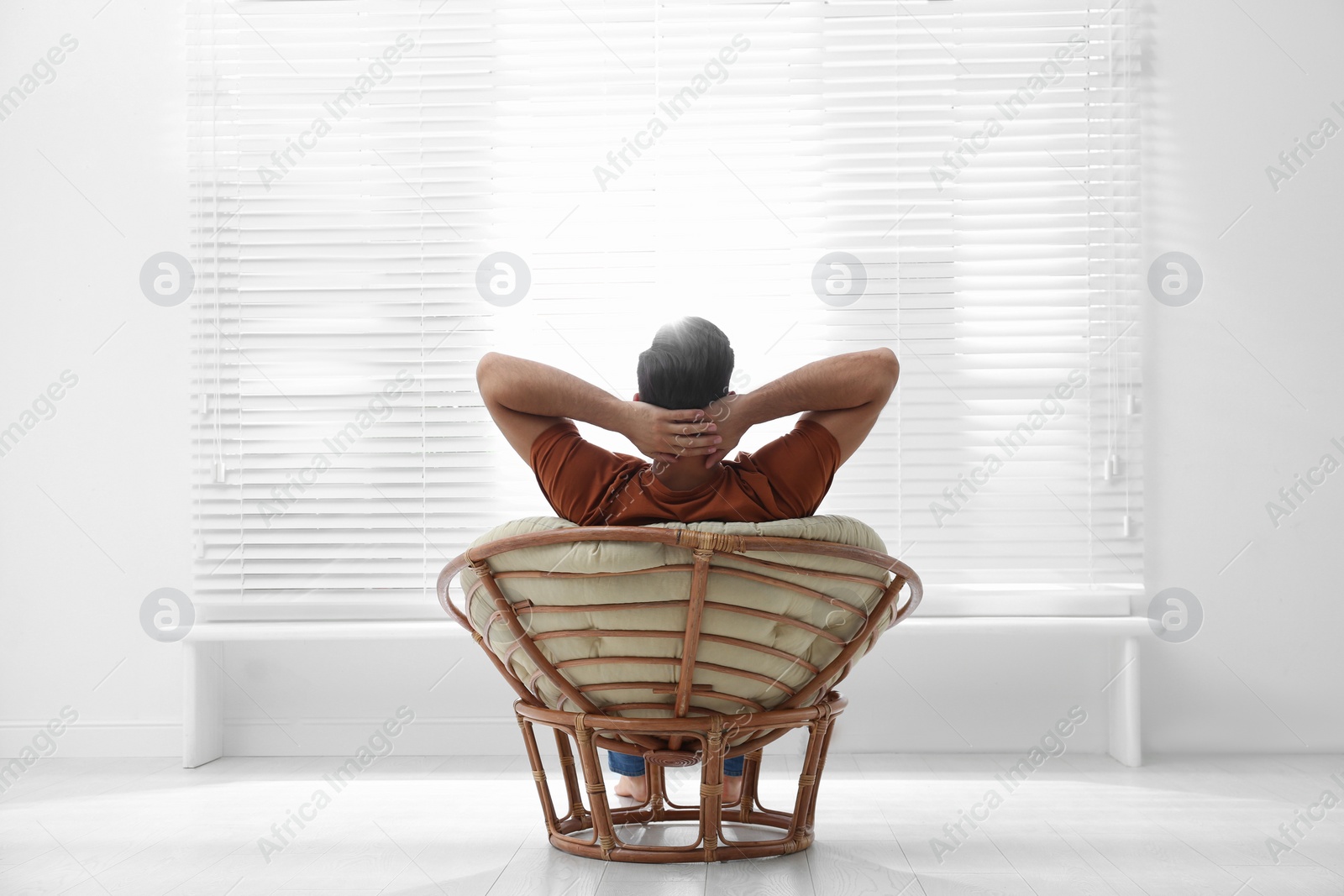 Photo of Man relaxing in papasan chair near window at home, back view