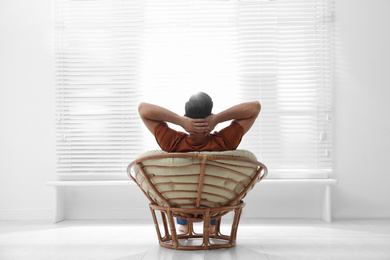 Man relaxing in papasan chair near window at home, back view