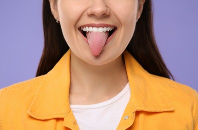 Photo of Happy young woman showing her tongue on purple background, closeup