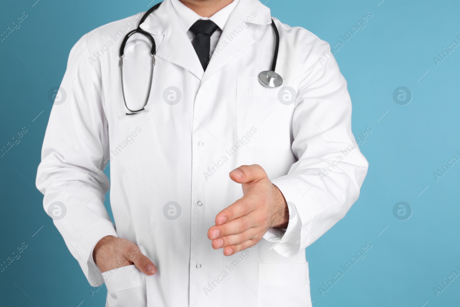 Photo of Doctor offering handshake on light blue background, closeup