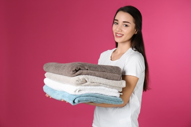 Happy young woman holding clean towels on color background. Laundry day