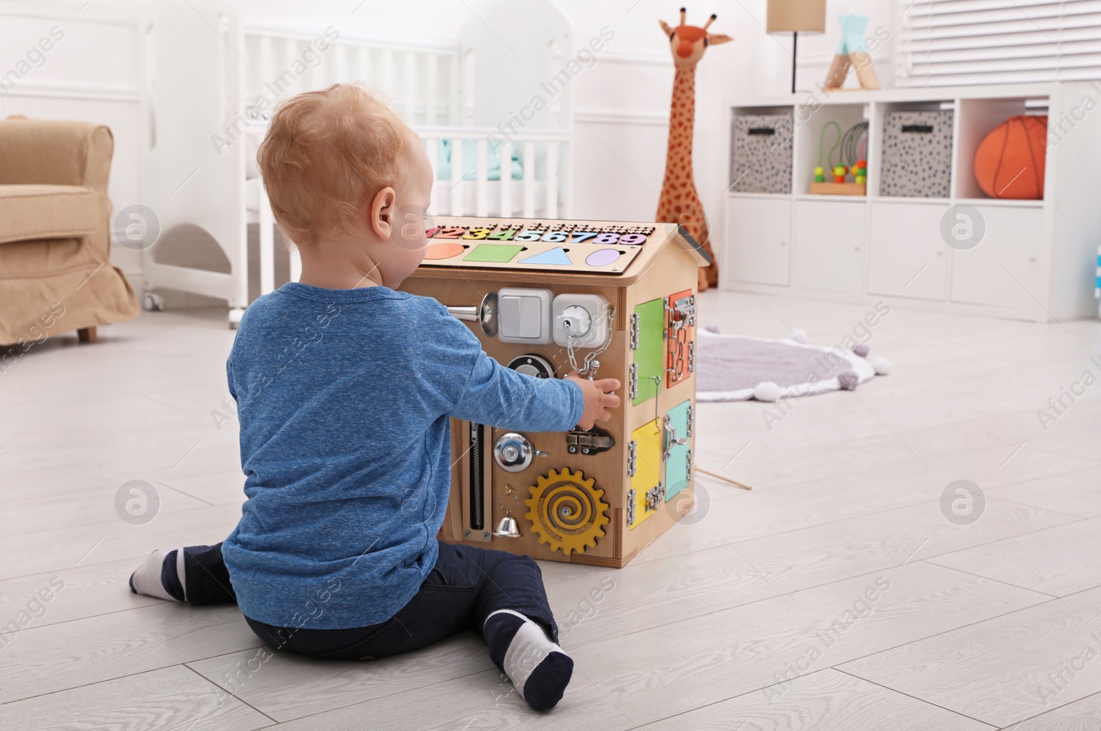 Photo of Cute little boy playing with busy board house on floor at home