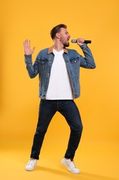 Photo of Handsome man with microphone singing on yellow background