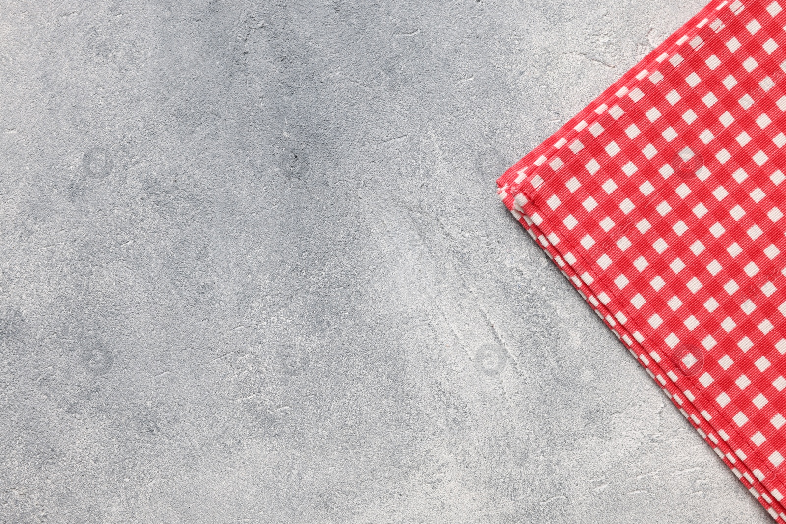 Photo of Red checkered tablecloth on light gray textured table, top view. Space for text