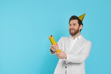 Happy man with party popper on light blue background. Space for text