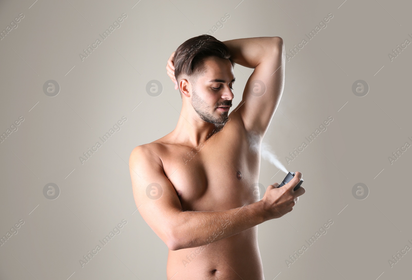 Photo of Young man using deodorant on gray background