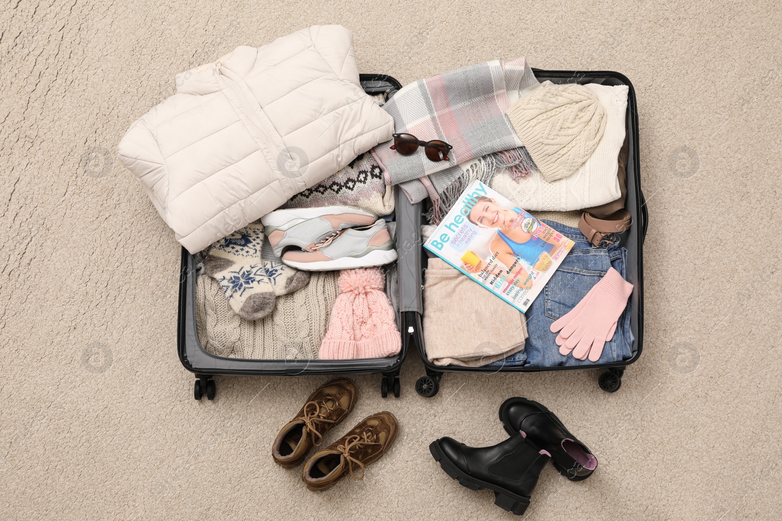 Photo of Open suitcase with warm clothes, accessories and shoes on floor, flat lay